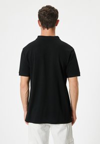 Sort polo skjorte med klassisk krave og korte ærmer, lavet af glat bomuldsstof, har en lige søm og minimal detaljering.