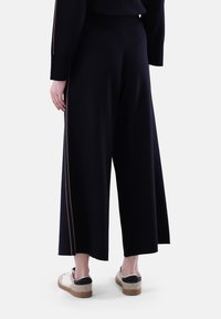 Helle schwarze Hose mit weitem Bein und dehnbarem Bund, versehen mit goldenen Seitenstreifen. Kombiniert mit hellen Sneakers mit schwarzen Akzenten.