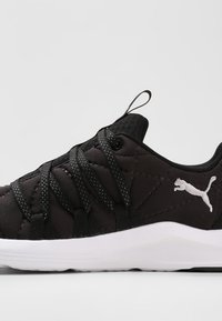 Svart sportskor med kviltad ovandel, intrikat snörningssystem, textil med struktur och vit gummisula med en liten logotyp.