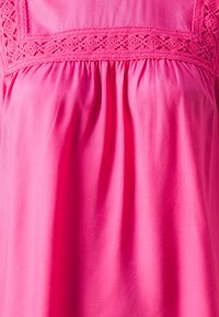 Blusa di cotone rosa con dettagli in pizzo intricati al colletto. Presenta una vestibilità ampia, una texture arricciata e un tessuto morbido e liscio.