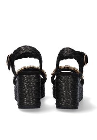 Sandalias de plataforma tejidas en negro con tacones gruesos y trenzados, adornadas con detalles de cuentas doradas y correas ajustables en el tobillo.