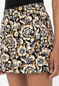 Jupe en tissu noir avec un grand motif floral jaune et blanc. Comprend une taille élastique et une étiquette avec le logo Dickies sur le côté.