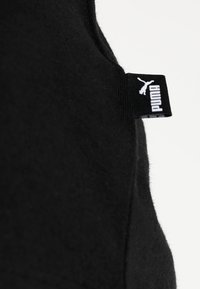 Textil negro con una textura suave que presenta una etiqueta rectangular blanca con "PUMA" y el logo en el lateral.