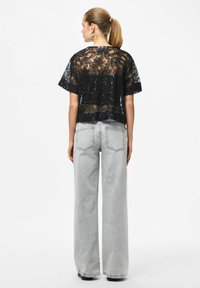 Črni čipkasti vrh s cvetličnim vzorcem in sequini, kombiniran s svetlo sivimi širokimi kavbojkami. Obleka je dopolnjena z ohlapnim krojem.