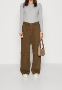 T shirt a maniche lunghe grigio chiaro con dettagli a bottoni, abbinato a pantaloni cargo marrone scuro a gamba larga con vita regolabile e una borsa beige.