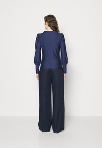 Navy blue blouse with puffed sleeves and a fitted body, paired with wide-leg navy trousers. Smooth texture, tailored design, minimal detailing.
