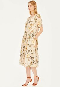 Beżowa sukienka do kolan z krótkim rękawem, z zabawnym nadrukiem różnych obiektów. Okrągły dekolt i boczne kieszenie. Cienka tekstura materiału.