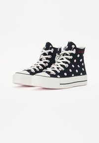 Baskets montantes avec une tige en toile noire ornée de pois roses, des lacets blancs et une semelle en caoutchouc blanche avec des accents noirs.