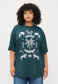 T-shirt oversize verde scuro con stampa grafica bianca raffigurante motivi tropicali e animali, tra cui una palma e leopardi.