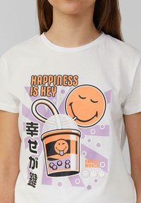 Witte t-shirt met korte mouwen, featuring een afbeelding van een lachende drinkbeker, een oranje lachend gezicht en de tekst "Happiness is Key" in vette letters.