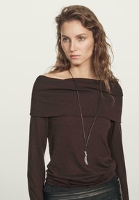 Braunes, schulterfreies Langarmoberteil mit Drapé-Design, aus weichem Stoff gefertigt, kombiniert mit einem schwarzen Lederrock und einer langen Anhängerhalskette.