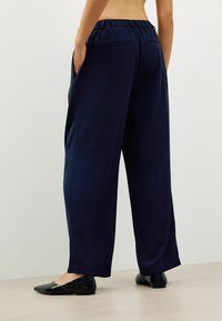 Marineblaue weit geschnittene Hosen mit elastischem Bund, ausgestattet mit zwei Gesäßtaschen und kombiniert mit schwarzen flachen Schuhen mit strukturiertem Finish.