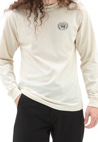 Cremefarbenes Langarmshirt mit rundem Ausschnitt, ausgestattet mit einem schwarzen Vans-Logo und Lorbeerdesign auf der Brust. Weicher Stoff, entspannte Passform.