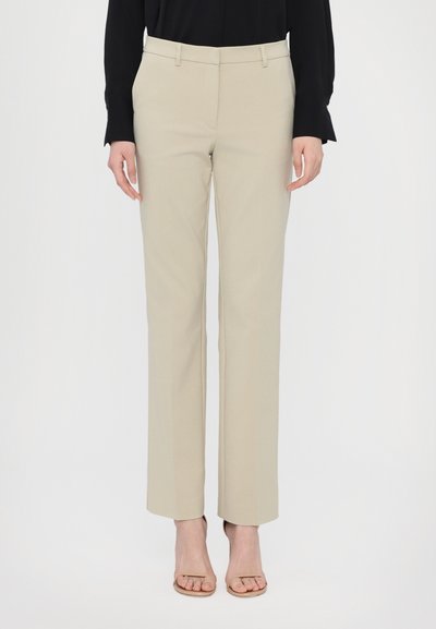 Pantaloni beige a gamba dritta con una texture liscia, caratterizzati da una vita media, passanti per la cintura e tasche laterali. Abbinati a sandali con tacco nude.