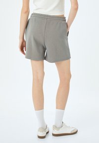 Grijze katoenen shorts van een blend met een elastische tailleband en zijzakken, met een ontspannen pasvorm en een gladde textuur. Draagt witte sneakers.