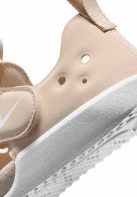 Μπεζ σαγιονάρα από αφρό με τρεις τρύπες αερισμού, ρυθμιζόμενο λουρί βέλκρο και χοντρή υφασμάτινη λευκή σόλα.
