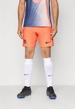 Nike fodboldoutfit med lyseorange shorts med et tekstureret mønster, et Barcelona-logo, hvide sokker og sorte støvler med blå accenter.