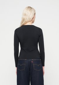 Top noir à manches longues en tissu doux, avec une coupe ajustée et un col rond. Associé à un jean à jambes larges bleu foncé.