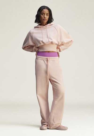 Light pink cropped hoodie with oversized sleeves, paired with light pink joggers featuring an elastic waistband and purple accents.