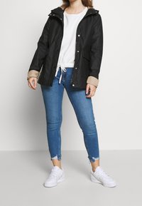 Czarna kurtka przeciwdeszczowa z kapturem, z wzorzystymi mankietami, zapinana na zamek i zatrzaski. Nosi się ją na białej bluzce i niebieskich, przetartych, obcisłych dżinsach, w zestawieniu z białymi trampkami.