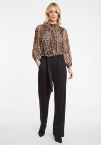 Woman wearing leopard print long-sleeve blouse with ruffled collar and black high-waisted wide-leg trousers with a waist tie.