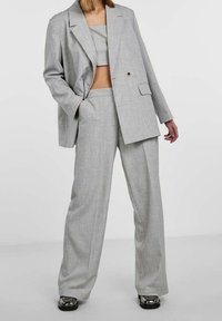 Szary luźny żakiet na dopasowanym, krótkim topie i szerokich spodniach. Tkanina ma subtelną fakturę, dopełnioną przez błyszczące czarne buty.