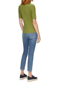 Olivengrünes kurzärmliges Oberteil, kombiniert mit hellblauen Skinny-Jeans und schwarzen Sneakers mit beiger Sohle. Glatter Stoff mit tailliertem Design.