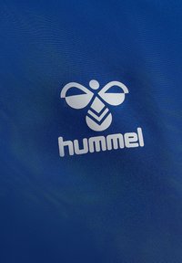 Blå tygbakgrund med en framträdande vit logotyp som har en symmetrisk bi-design ovanför ordet "hummel" i fet stil.