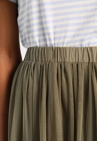 Camiseta de rayas azul claro y blancas combinada con una falda de tul verde oliva fruncida, que cuenta con una cintura elástica y una textura suave y translúcida.