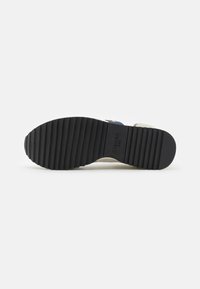 Suola di scarpa in gomma con una struttura a motivi. Presenta una tomaia di colore chiaro e una fascia di accentuazione blu. Robusta e con una texture per una buona aderenza.