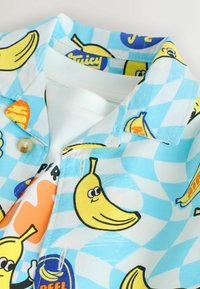 Hellblau-weiß kariertes Hemd mit Cartoon-Bananen und fruchtbezogenen Designs auf einem weißen Innenhemd.