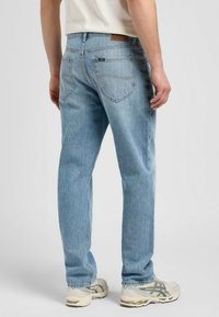 Ljusblå denimjeans med rak bendesign, som har en läderlapp, bakfickor och enkla sömnadsdetaljer.