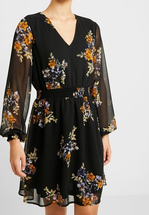Robe noire à motif floral avec des manches longues en tissu transparent, un col en V, une taille élastique, et des motifs de fleurs orange, violettes et beiges sur un tissu fluide.