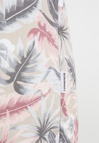Camisa de tela ligera con un patrón de hojas tropicales en rosa, gris y beige; etiqueta de marca con "Lindbergh" mostrada en el lado.