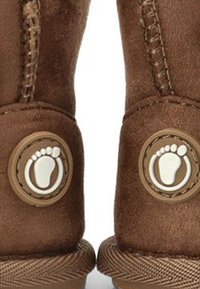 Botas de ante marrón con acentos circulares y huellas blancas, suelas texturizadas y costuras detalladas a lo largo de los lados.