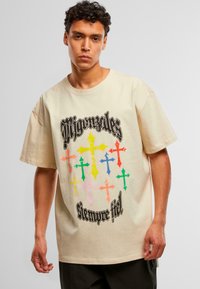 Camiseta de algodón beige con un corte relajado que presenta cruces multicolores y un diseño de texto negro en la parte frontal.