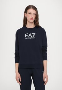Tengerészkék pulóver kerek nyakkal, fehér EA7 Emporio Armani logóval. Puha tapintású, hosszú ujjú, illeszkedő nadrággal párosítva.