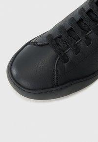 Gros plan sur une chaussure noire en cuir à lacets, mettant en évidence des coutures détaillées et un bout rond texturé sur fond blanc.