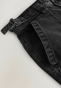 Gros plan sur un pantalon en denim noir avec une poche latérale et une ceinture en tissu munie d'une boucle rectangulaire en métal.
