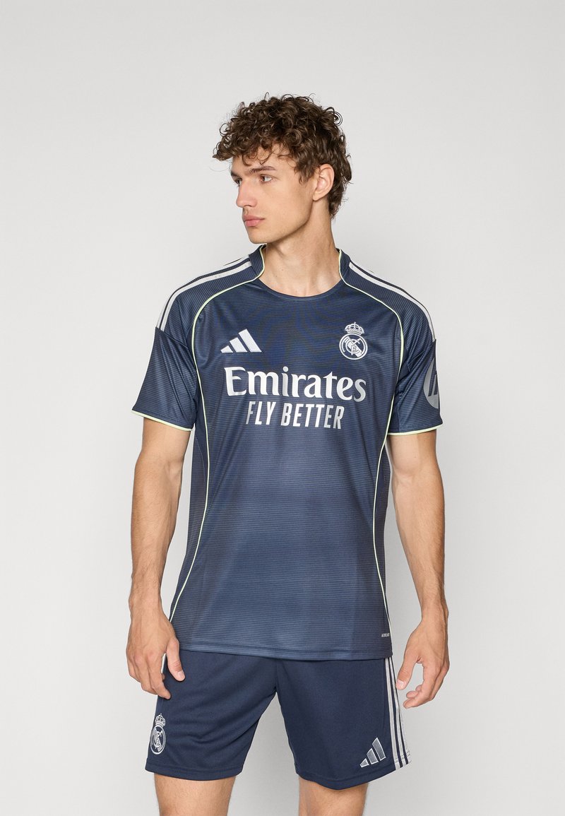 Maillot de Real Madrid bleu marine avec des rayures horizontales, logo Adidas blanc, et texte "Emirates Fly Better". Accompagné de shorts assortis.