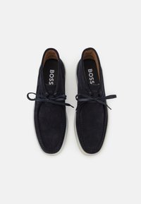 Navy suede boat shoes with a rounded toe, lace-up design, and cream rubber sole. Features tonal stitching and branded insole.