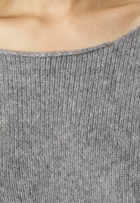 Grijze gebreide sweaterstof met een geribbelde textuur en een brede halslijn. Het materiaal lijkt zacht, warm en iets loszittend.