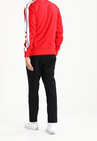 Rød sweatshirt med hvide skulderstriber, ribbede ærmekanter og rund halsudskæring, kombineret med sorte bukser og hvide sneakers. Enkel, afslappet stil.