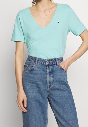 Hemelsblauw katoenen T-shirt met een brede V-hals en korte mouwen, gecombineerd met hooggetailleerde, loszittende blauwe denim jeans. Klein logodetail zichtbaar.