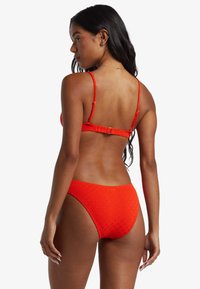 Bikini rosso con un motivo texture, spalline regolabili e chiusura con gancio sul retro. Il design presenta uno slip a vita alta.