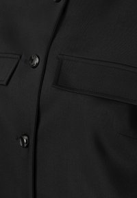 Schwarzes Hemd mit Knopfleiste, aus glattem Stoff, mit metallischen Knöpfen und zwei aufgesetzten Taschen vorne mit abgesteppten Kanten.