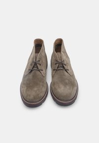 Stivali alla caviglia in suede marrone con punta rotonda, dotati di suola in gomma, chiusura con lacci e dettagli di cucitura in contrasto.