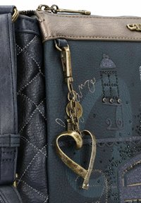 Dunkelblaue Lederhandtasche mit gestepptem Muster, metallischen Akzenten, dekorativem Schlüsselanhänger und geprägten Designs auf der Vorderseite.