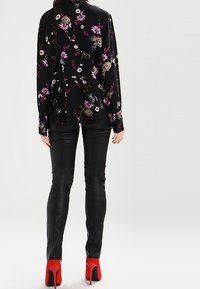 Blouse noire à manches longues avec des fleurs roses et blanches, associée à un pantalon noir ajusté et des chaussures à talons rouges. Textures lisses visibles.
