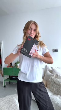 T-shirt feminina Perfect V-neck da Levi's em branco, apresentada em embalagem que destaca o seu corte descontraído. Modelo veste calças pretas, em ambiente interno com acabamentos suaves.